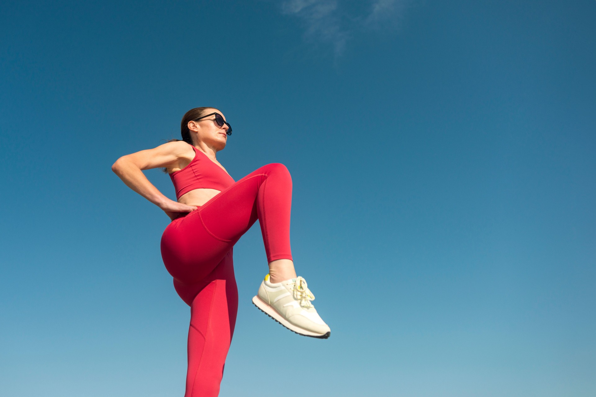 Sporty female is doing warm up exercises and stretching outdoors. Red sports clothing