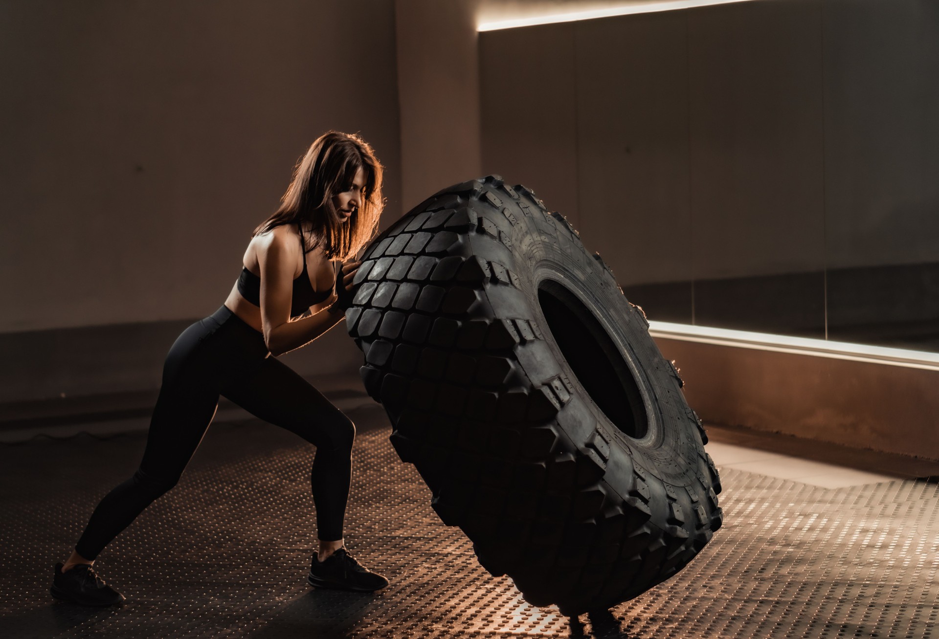 In a dynamic gym setting, a strong woman engages in rigorous training, showcasing her impressive tire flip technique. This exercise epitomizes her dedication to fitness and strength improvement