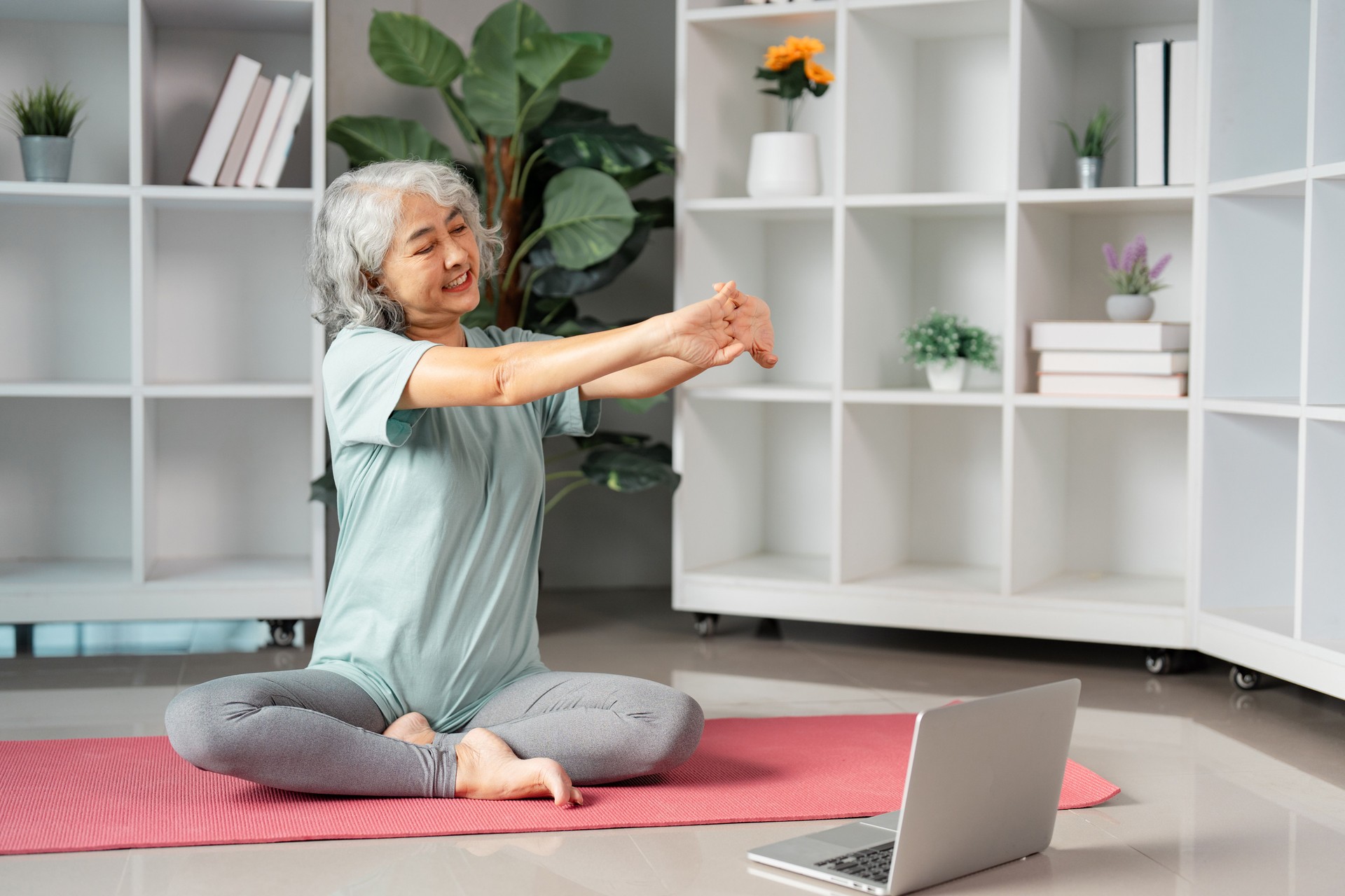 Senior woman practicing yoga and stretching at home with online guidance